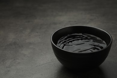 Photo of Black bowl with water on grey table. Space for text