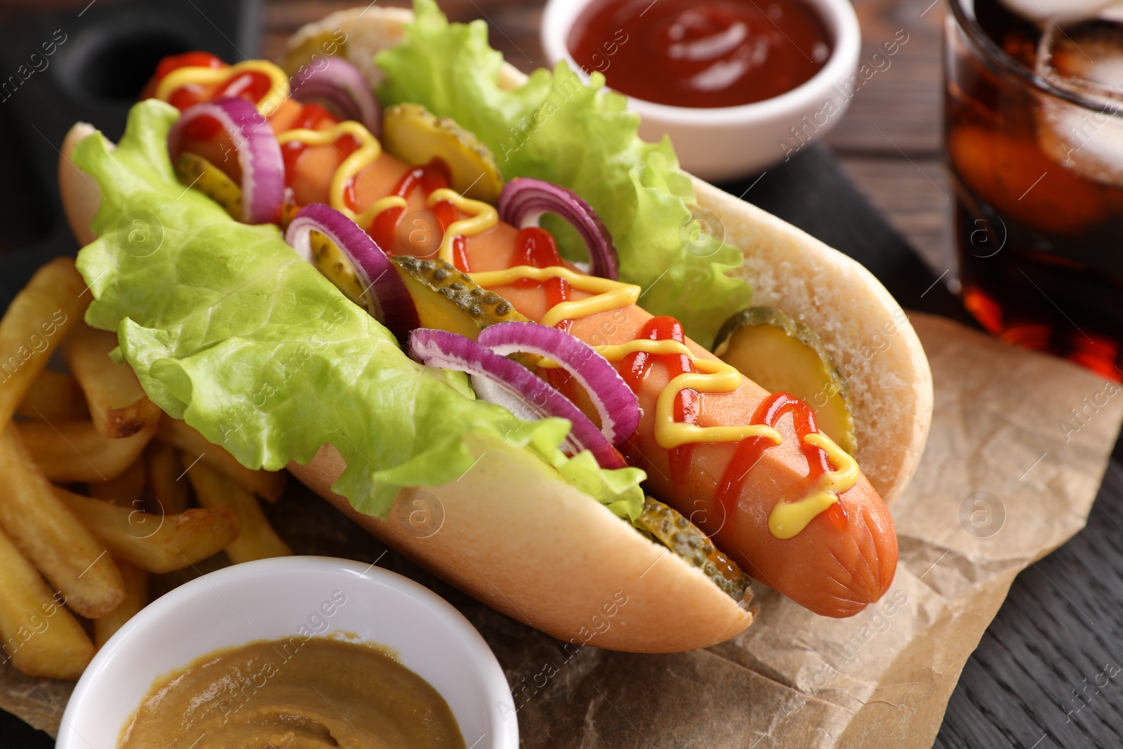 Photo of Delicious hot dog with lettuce, onion and pickle served on wooden table, closeup