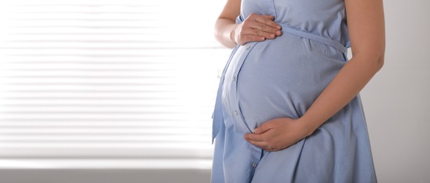 Image of Young pregnant woman near window indoors, closeup view with space for text. Banner design