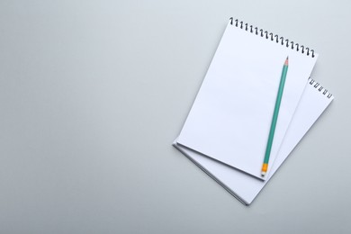 Photo of Notebooks and pencil on light grey background, top view. Space for text
