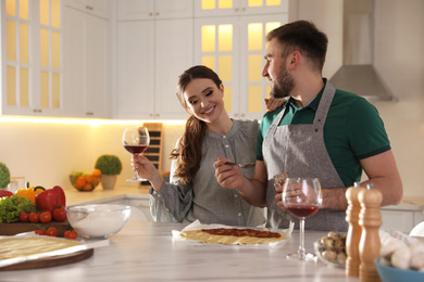 Photo of Lovely young couple cooking pizza together in kitchen