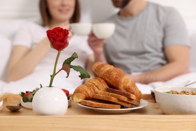 Photo of Tasty breakfast on tray, closeup. Happy couple drinking coffee in bed, selective focus