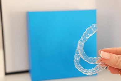 Photo of Woman with transparent dental aligners on blurred background, closeup. Space for text