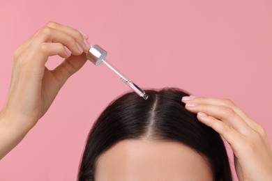 Photo of Woman applying hair serum on pink background, closeup. Cosmetic product
