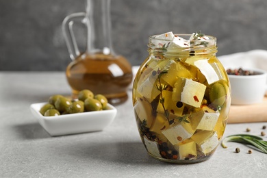 Photo of Jar with feta cheese marinated in oil on light grey table. Pickled food