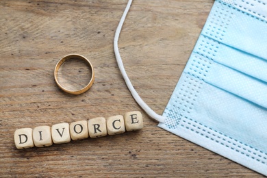 Photo of Flat lay composition with protective mask and wedding ring on wooden table. Divorce during coronavirus quarantine