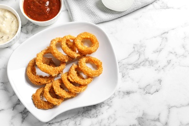 Photo of Homemade crunchy fried onion rings with sauces on marble table, top view. Space for text