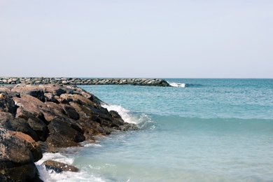 Picturesque view of beautiful rocky beach with breakwater on sunny day