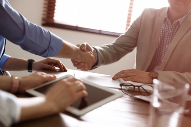 Photo of Business partners shaking hands at table after meeting in office, closeup