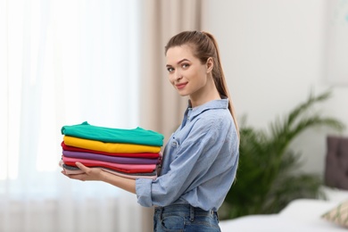 Photo of Woman holding folded clean clothes in bedroom. Laundry day