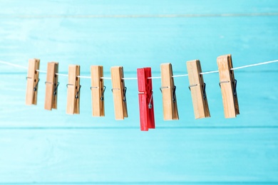 Photo of One different clothes peg among others hanging on rope against color background
