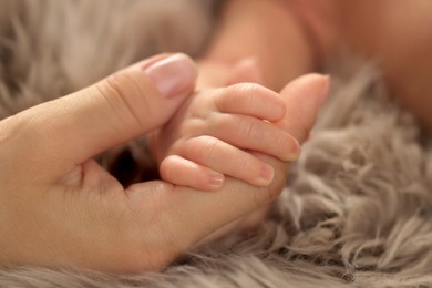 Photo of Mother holding hand of her newborn baby on fluffy blanket, closeup. Lovely family