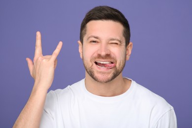 Photo of Happy man showing his tongue and rock gesture on purple background