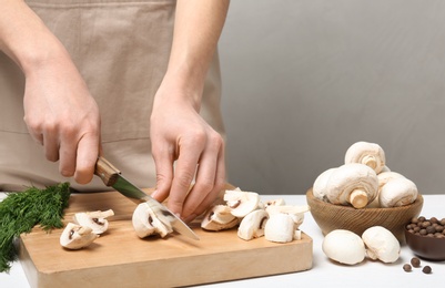 Photo of Young woman cutting fresh champignon mushrooms on wooden board, closeup view. Space for text