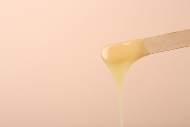 Photo of Wooden spatula with hot depilatory wax on beige background. Space for text