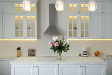 Photo of Peony bouquet on white marble table in kitchen interior