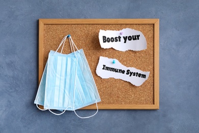 Photo of Paper pieces with phrase Boost your Immune System and medical face masks pinned to corkboard on blue wall