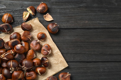 Photo of Tasty roasted edible chestnuts on black wooden table, flat lay. Space for text