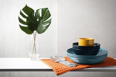 Photo of Set of clean dishware, cutlery and tropical leaves on white table