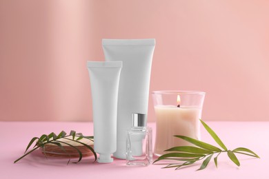 Photo of Different hand care cosmetic products, candle and green leaves on pink background