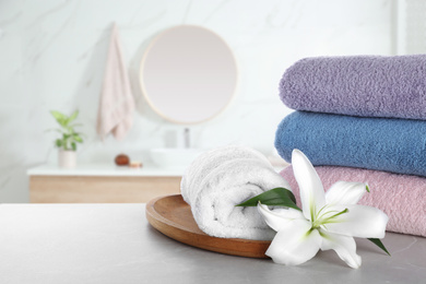 Image of Fresh towels and lily flower on grey table in bathroom. Space for text