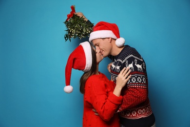 Photo of Happy couple kissing under mistletoe bunch on light blue background