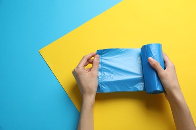 Photo of Woman holding roll of light blue garbage bags over color background, top view. Space for text