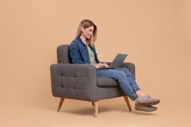 Photo of Happy woman with laptop sitting in armchair on beige background