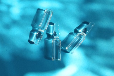 Photo of Skincare ampoules in sunlight on light blue background, top view