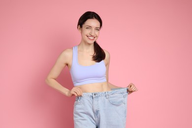 Photo of Happy young woman in big jeans showing her slim body on pink background
