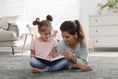 Photo of Young mother and her daughter reading book on floor at home