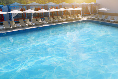 Image of Lounge chairs with umbrellas near swimming pool on sunny day 