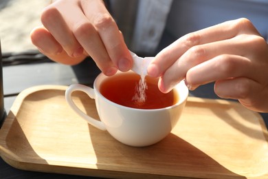 Photo of Woman adding sugar into cup of tea at table, closeup