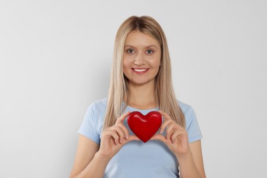 Photo of Happy volunteer holding red heart with hands on light background