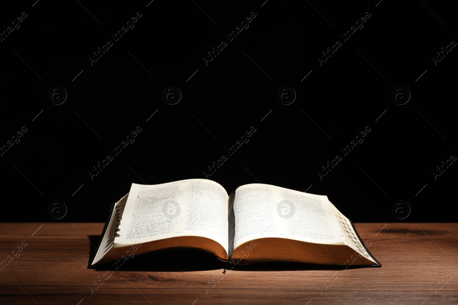 Photo of Open Bible on wooden table against black background. Christian religious book
