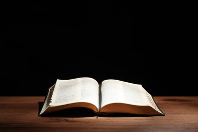 Photo of Open Bible on wooden table against black background. Christian religious book