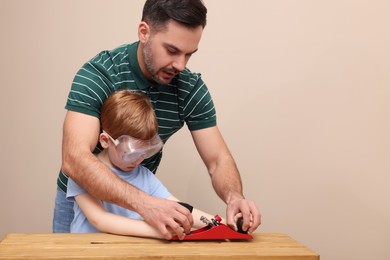 Photo of Father teaching son how to work with plane near beige wall