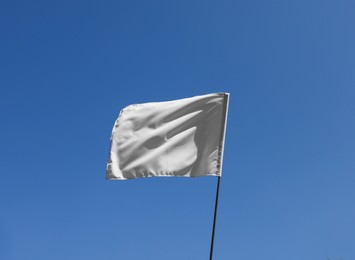 Photo of White flag fluttering against blue sky on sunny day