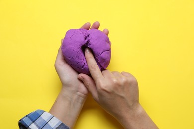Photo of Woman playing with kinetic sand on yellow background, top view