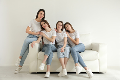 Photo of Beautiful young ladies in jeans and white t-shirts on sofa indoors. Woman's Day