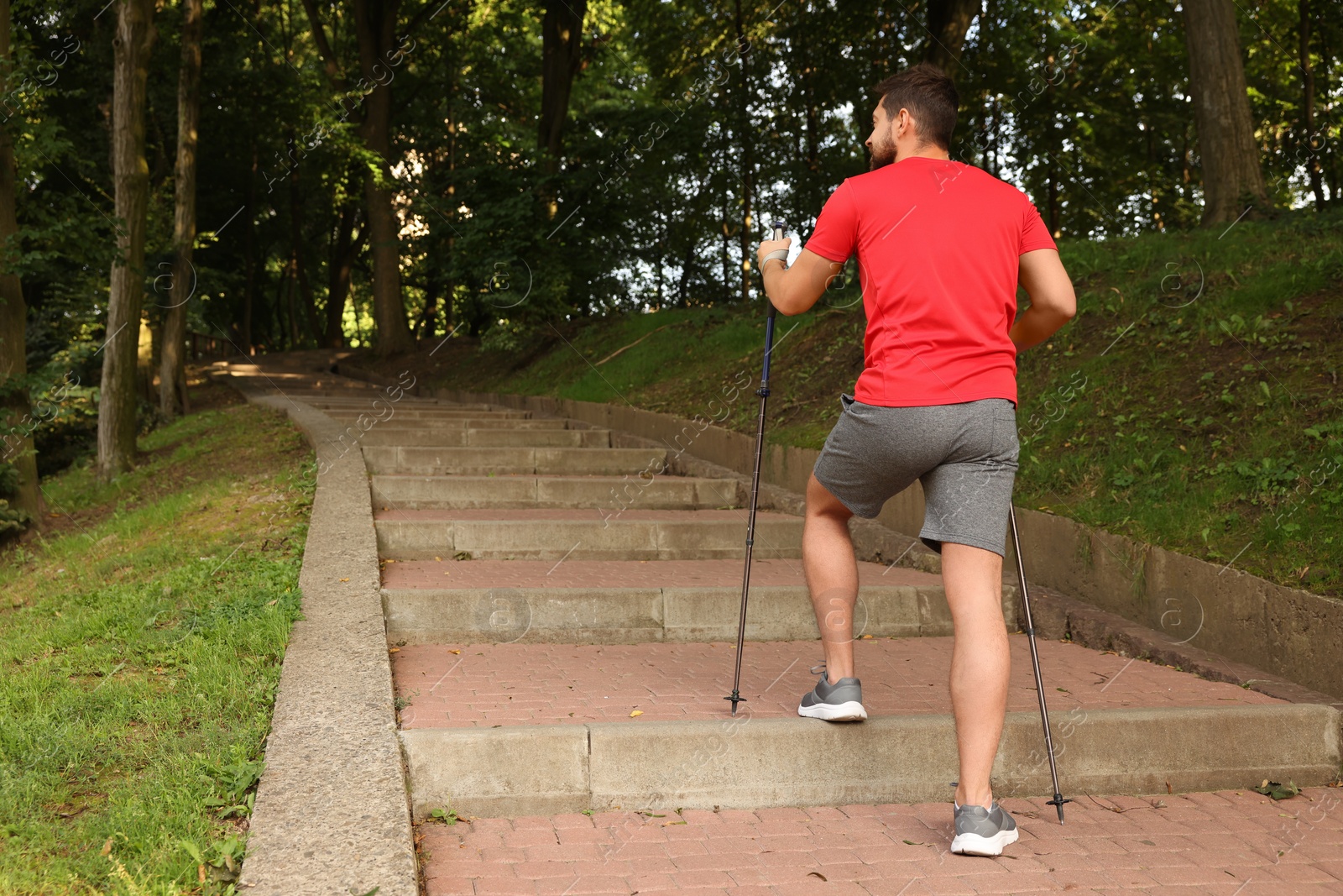 Photo of Man practicing Nordic walking with poles on steps outdoors, back view. Space for text