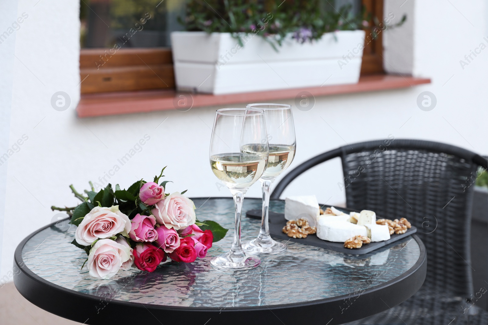 Photo of Bouquet of roses, glasses with wine and food on glass table near house on outdoor terrace
