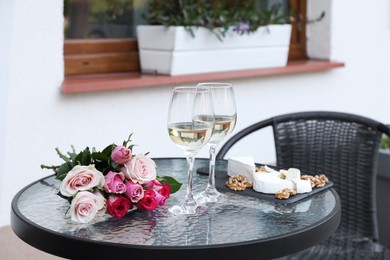 Photo of Bouquetroses, glasses with wine and food on glass table near house on outdoor terrace