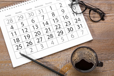 Photo of Flat lay composition with calendar and cup of coffee on wooden table