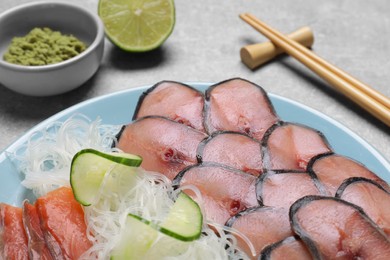 Photo of Set with raw salmon and mackerel slices served with cucumber, funchosa and vasabi on light grey table, closeup