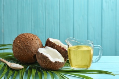 Photo of Jug of natural organic oil and coconuts on blue wooden table. Space for text