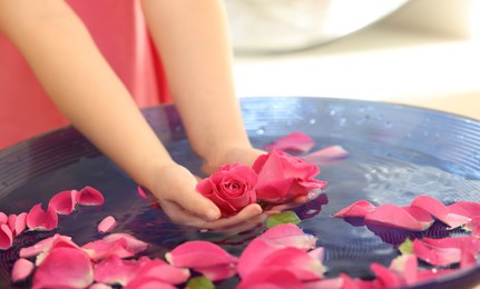Photo of Child holding rose flower in bowl with water and petals on blurred background, closeup
