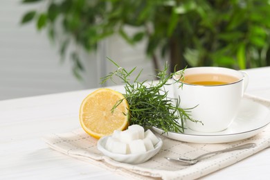 Photo of Aromatic herbal tea, fresh tarragon sprigs, sugar cubes and lemon on white wooden table, space for text