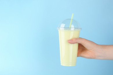 Photo of Woman with plastic cup of tasty smoothie on light blue background, closeup. Space for text