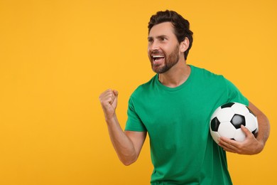 Photo of Emotional sports fan with soccer ball on orange background, space for text